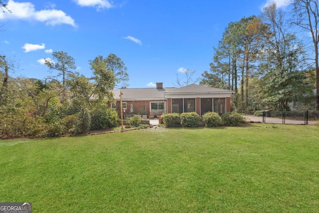 rear view of property with fence, a yard, a sunroom, brick siding, and a chimney