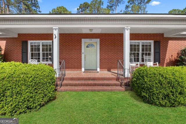 view of exterior entry with a yard, brick siding, and covered porch