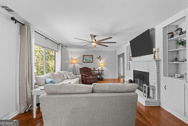 living room featuring visible vents, a brick fireplace, built in shelves, dark wood finished floors, and a ceiling fan