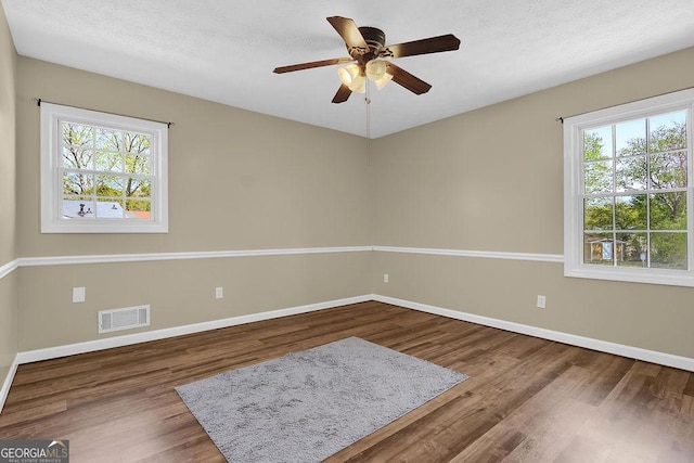 spare room featuring baseboards, visible vents, a healthy amount of sunlight, and wood finished floors