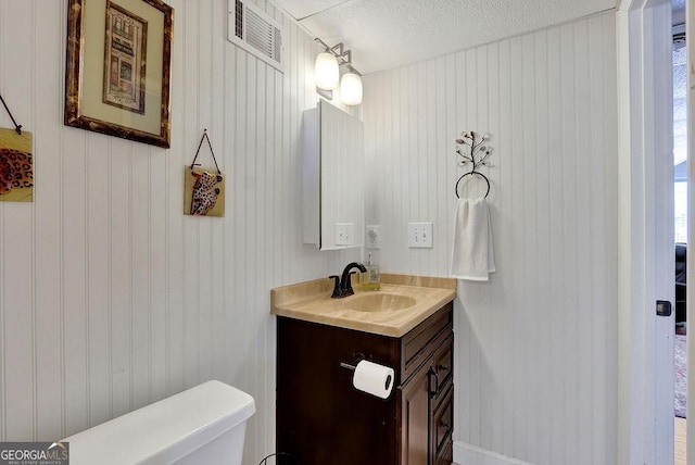 bathroom with a textured ceiling, visible vents, toilet, and vanity