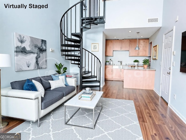 living area featuring visible vents, dark wood-type flooring, a towering ceiling, and stairway