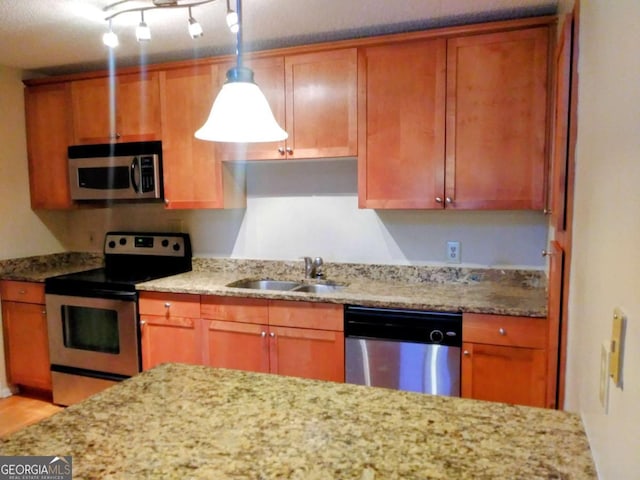 kitchen featuring light stone countertops, pendant lighting, appliances with stainless steel finishes, brown cabinetry, and a sink