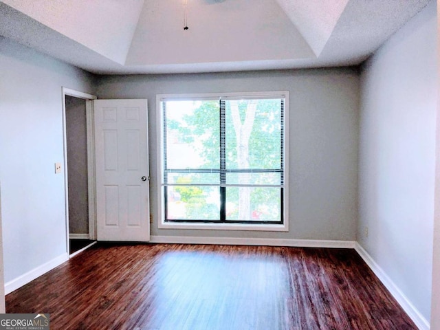 spare room featuring dark wood-style floors, baseboards, lofted ceiling, a textured ceiling, and a raised ceiling