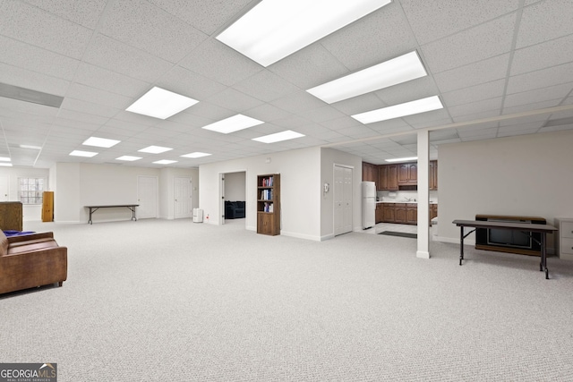 below grade area featuring a paneled ceiling, baseboards, light carpet, and freestanding refrigerator