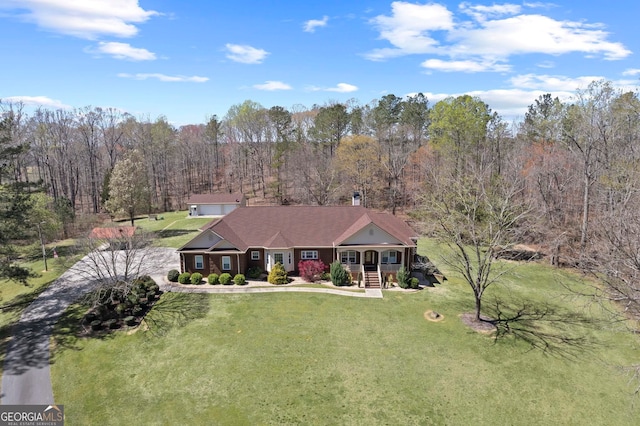 view of front of house featuring driveway, a view of trees, covered porch, a front yard, and a chimney