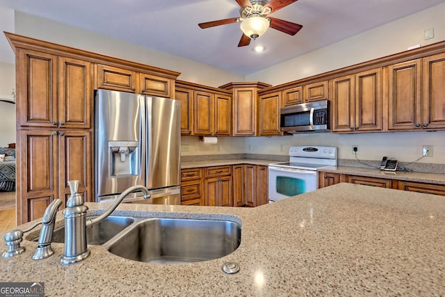 1068 Coleman River Rd, Clayton, GA 30525 - kitchen featuring appliances with stainless steel finishes, brown cabinets, a ceiling fan, a sink, and light stone counters