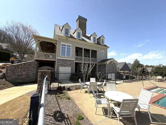 back of property with stone siding, a patio, fence, a community pool, and a balcony