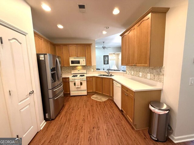 kitchen featuring a sink, tasteful backsplash, wood finished floors, white appliances, and light countertops