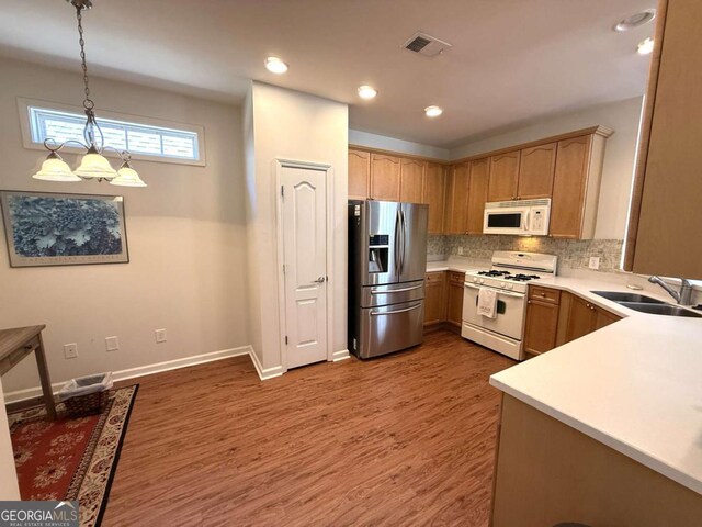kitchen with visible vents, a sink, wood finished floors, white appliances, and decorative backsplash