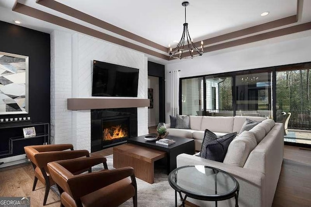 living room with a chandelier, a raised ceiling, a brick fireplace, and wood finished floors