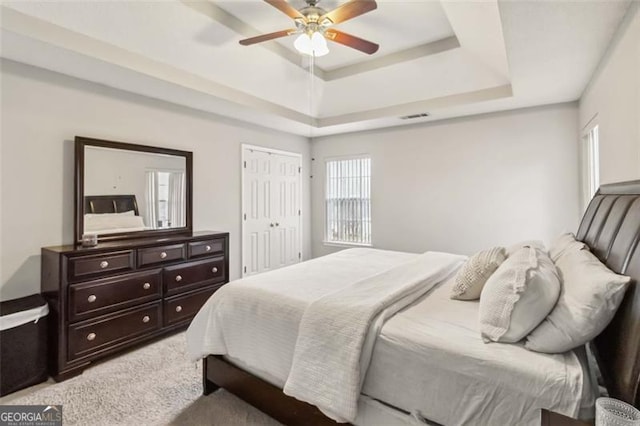 bedroom with visible vents, light carpet, a closet, a raised ceiling, and ceiling fan