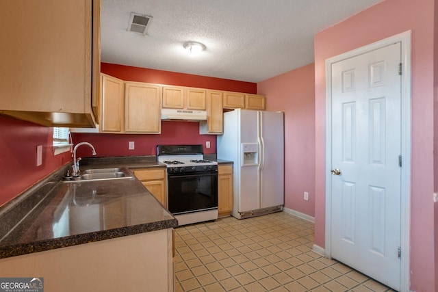 kitchen with dark countertops, under cabinet range hood, a sink, white refrigerator with ice dispenser, and gas range oven