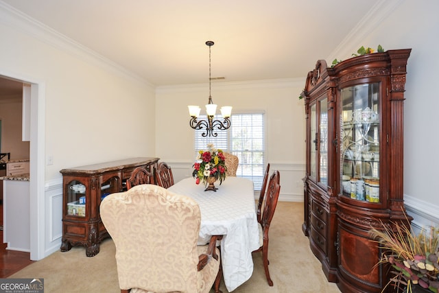 dining room featuring a wainscoted wall, ornamental molding, a decorative wall, light colored carpet, and a chandelier