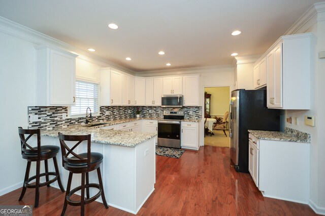 kitchen featuring a sink, white cabinetry, stainless steel appliances, a peninsula, and light stone countertops