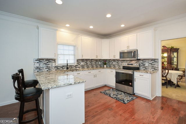 kitchen featuring white cabinetry, a peninsula, a kitchen breakfast bar, and appliances with stainless steel finishes