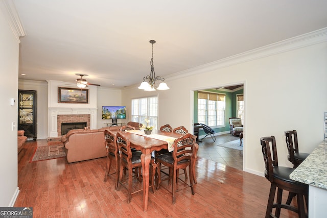 dining area with ornamental molding, a ceiling fan, wood finished floors, a fireplace, and baseboards