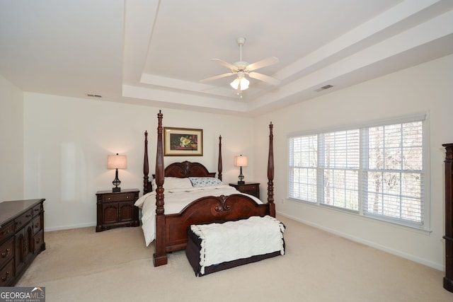 bedroom with visible vents, baseboards, light colored carpet, a raised ceiling, and a ceiling fan