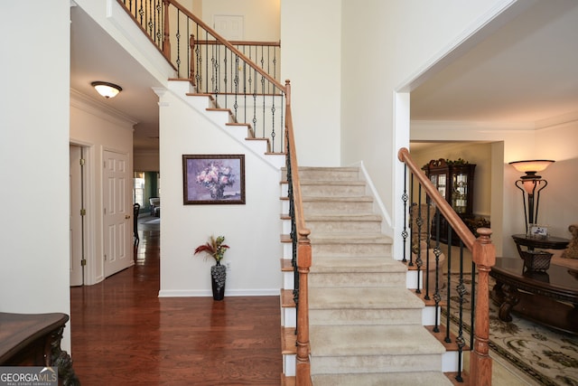 stairway with a towering ceiling, baseboards, wood finished floors, and crown molding