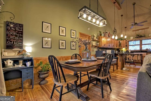 dining space with a wainscoted wall, ceiling fan, wood walls, a towering ceiling, and light wood-type flooring