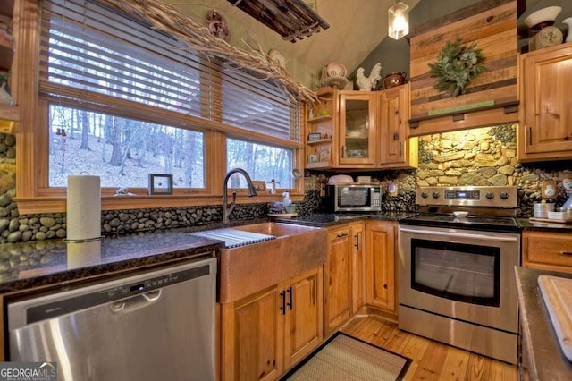 kitchen featuring dark stone countertops, a sink, glass insert cabinets, light wood-style floors, and appliances with stainless steel finishes