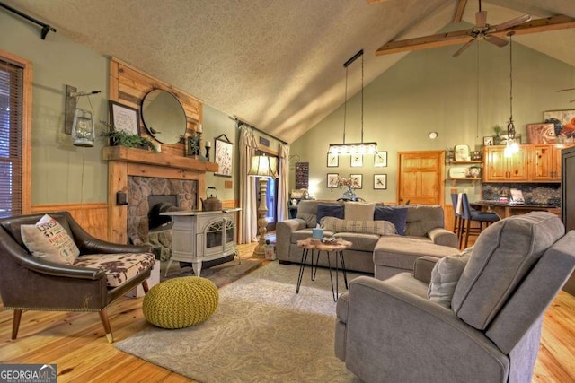 living area with wood finished floors, high vaulted ceiling, a wood stove, ceiling fan, and a textured ceiling