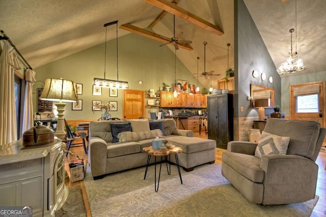 living area featuring light wood-type flooring, a wainscoted wall, beam ceiling, high vaulted ceiling, and ceiling fan with notable chandelier