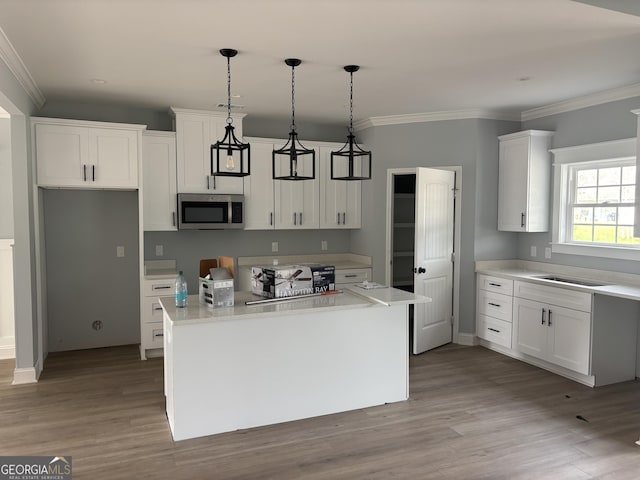 117 Rachel Way, Brunswick, GA 31523 - kitchen with stainless steel microwave, a kitchen island, white cabinets, wood finished floors, and ornamental molding