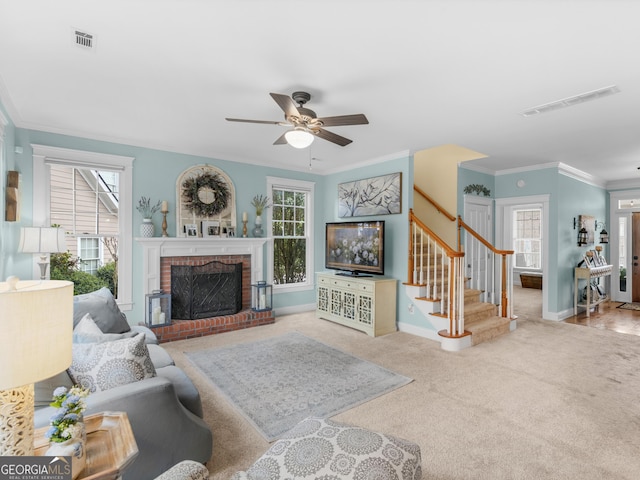 carpeted living area featuring visible vents, a brick fireplace, stairway, ornamental molding, and a ceiling fan