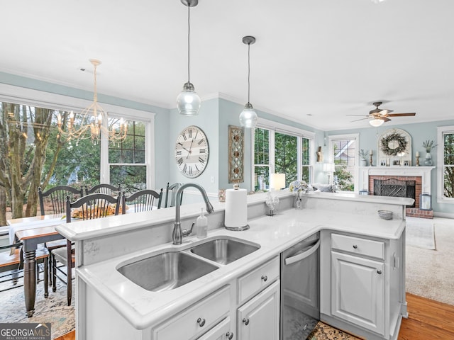 kitchen with a ceiling fan, a sink, stainless steel dishwasher, light countertops, and a brick fireplace