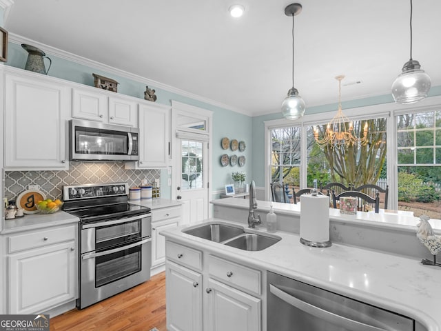 kitchen featuring a sink, ornamental molding, stainless steel appliances, white cabinetry, and a chandelier