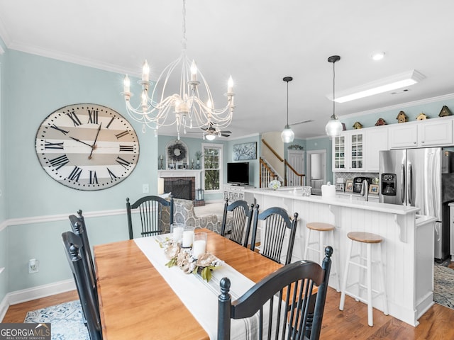 dining room featuring a fireplace, light wood-type flooring, an inviting chandelier, and ornamental molding