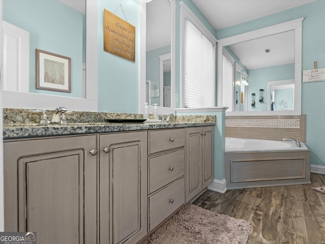 bathroom featuring double vanity, a garden tub, wood finished floors, and a sink