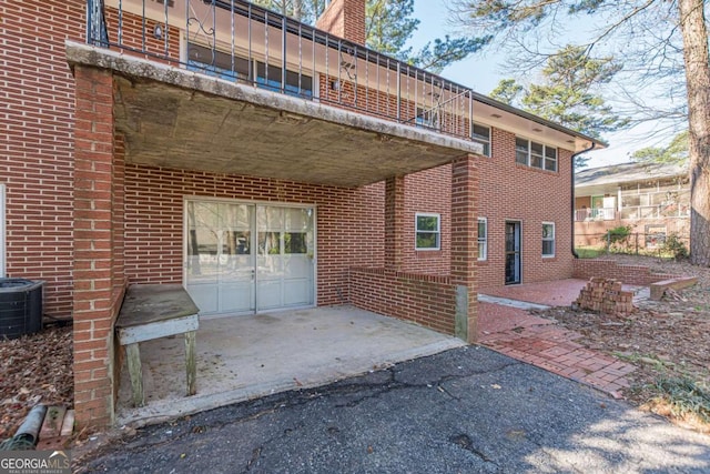 view of side of property featuring brick siding, cooling unit, aphalt driveway, and a balcony