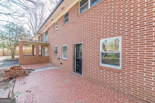 back of house featuring a patio, a balcony, and brick siding