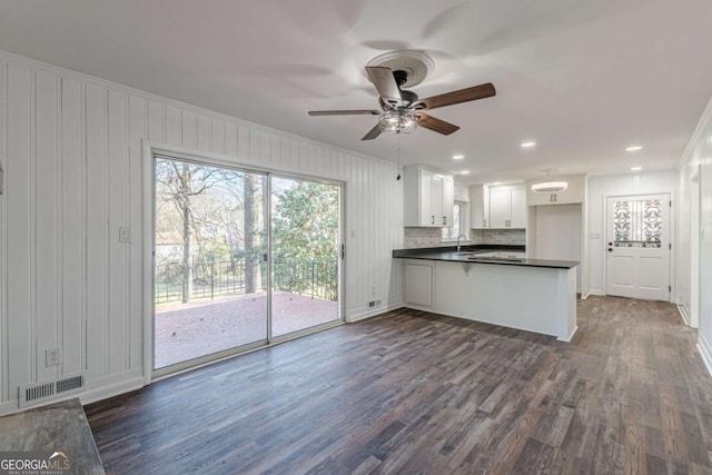 kitchen with dark countertops, visible vents, dark wood-type flooring, a peninsula, and a ceiling fan