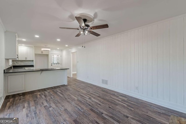 kitchen with dark wood-type flooring, dark countertops, a peninsula, and a ceiling fan