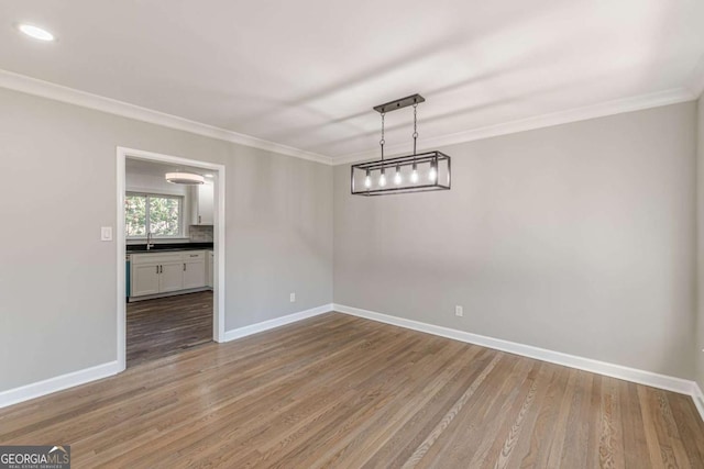 unfurnished dining area featuring crown molding, wood finished floors, baseboards, and a sink
