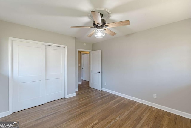 unfurnished bedroom featuring wood finished floors, baseboards, and a closet
