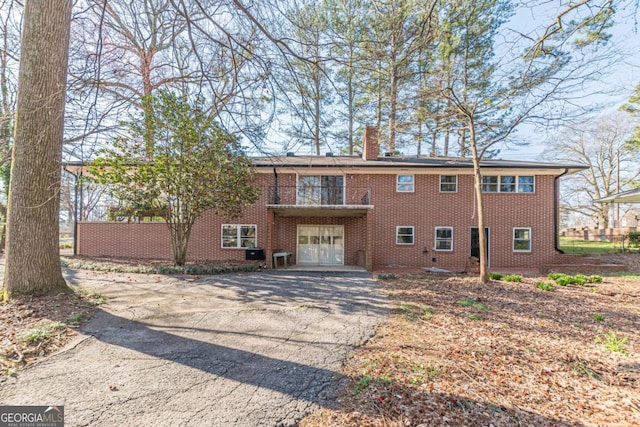 view of front of home featuring an attached garage, a chimney, french doors, aphalt driveway, and brick siding