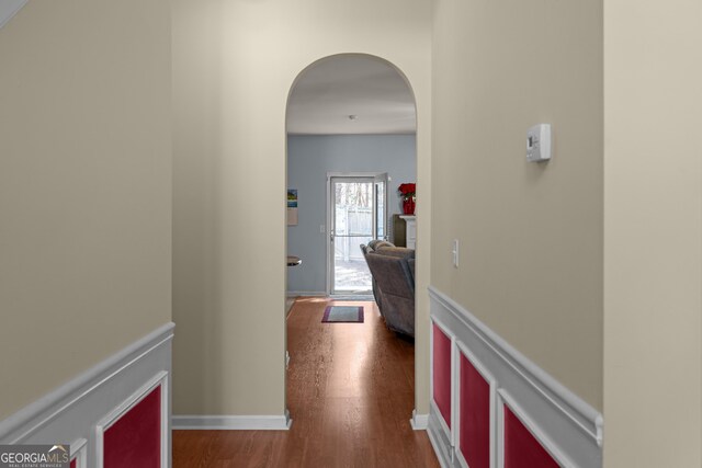 hall featuring arched walkways, dark wood finished floors, and baseboards