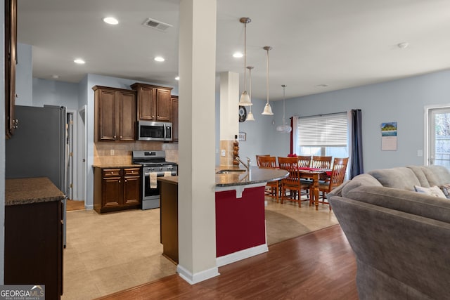 kitchen with visible vents, open floor plan, a kitchen bar, a peninsula, and stainless steel appliances
