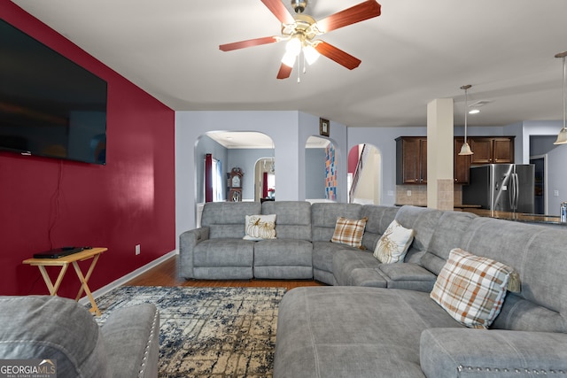 living room featuring a ceiling fan, wood finished floors, arched walkways, and baseboards