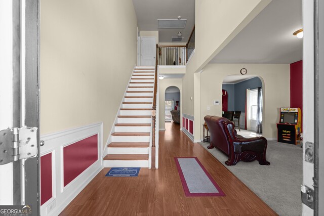 entrance foyer featuring wood finished floors, stairway, arched walkways, baseboards, and a towering ceiling