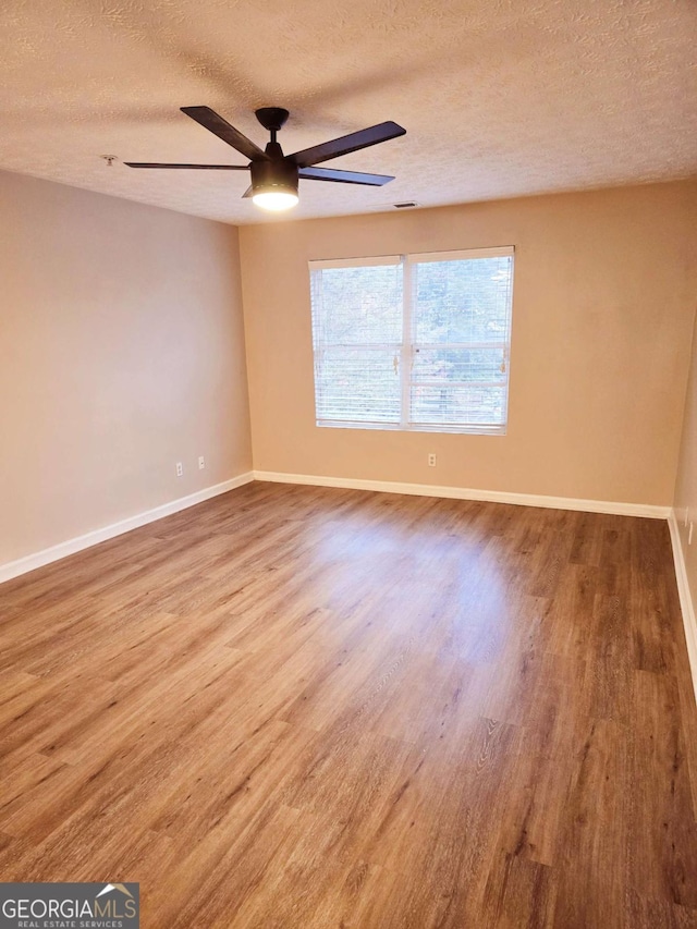 empty room featuring a textured ceiling, baseboards, a ceiling fan, and wood finished floors