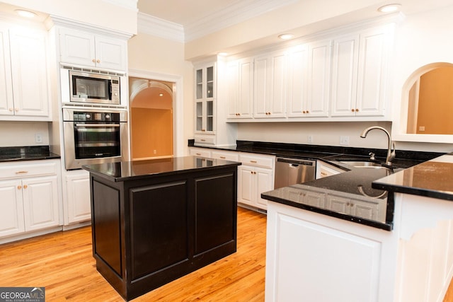 kitchen with a sink, stainless steel appliances, ornamental molding, and white cabinetry