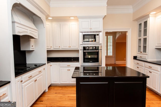 kitchen with light wood-type flooring, custom range hood, ornamental molding, appliances with stainless steel finishes, and white cabinets