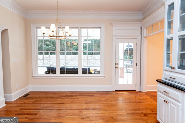 unfurnished dining area featuring visible vents, a notable chandelier, ornamental molding, light wood finished floors, and baseboards