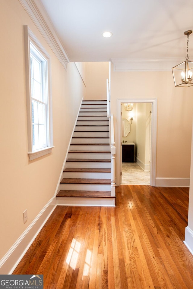 stairway featuring baseboards, a chandelier, hardwood / wood-style floors, ornamental molding, and recessed lighting