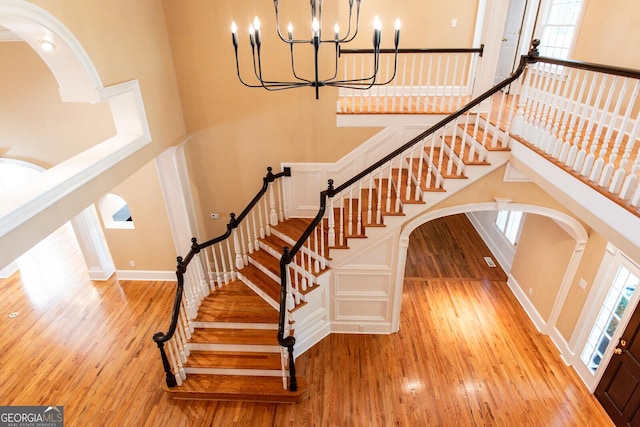 stairway featuring arched walkways, a notable chandelier, a high ceiling, and wood finished floors